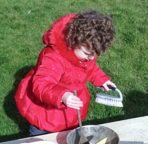 Photograph of a girl in a red coat washing up play at Longscroft Nursery